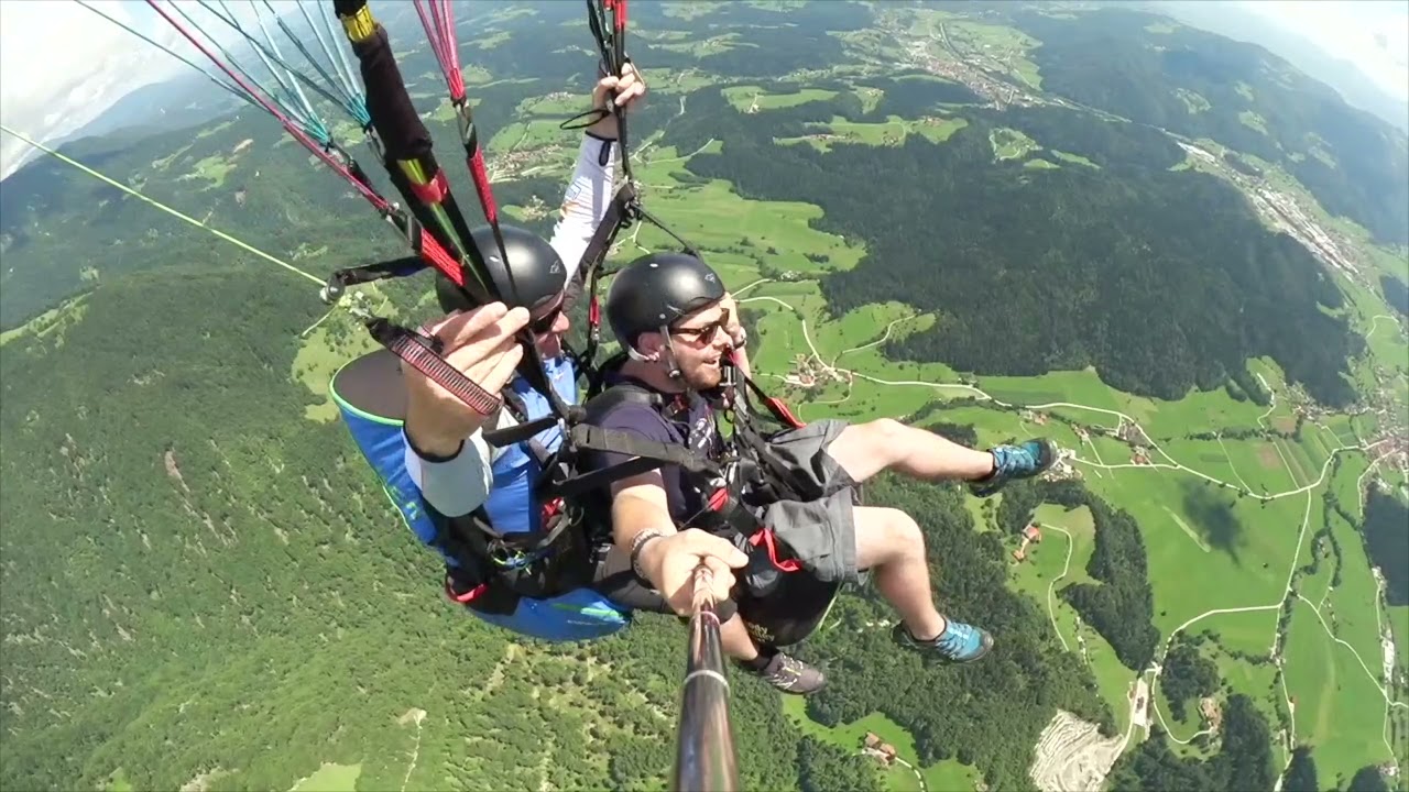Tandemski pilot in potnik med poletom z jadralnim padalom nad zeleno alpsko dolino